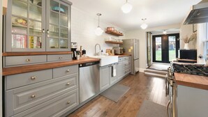 Eine moderne Küche mit grauen Schränken, Holz Arbeitsplatten und Edelstahlgeräten. Hängende Pendelleuchten und ein Einbauofen sind vorhanden.