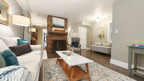 Ein Wohnzimmer mit Kamin, einem weißen Sofa, einem Couchtisch und einem gemusterten Teppich.