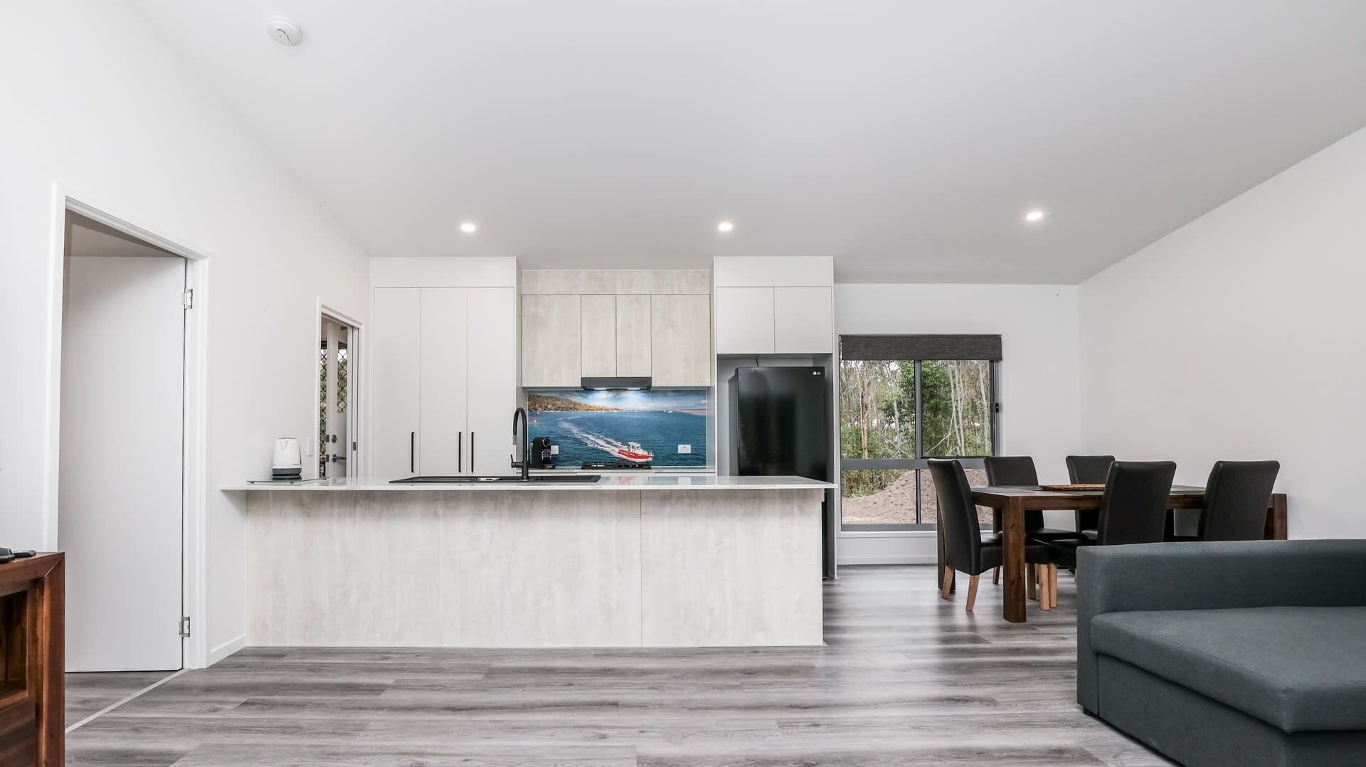 Cozinha moderna com ilha central, área de jantar com mesa e cadeiras, e uma grande janela com vista para o exterior.