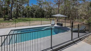 Una piscina rettangolare con recinzione in metallo nero, circondata da un prato e alberi.