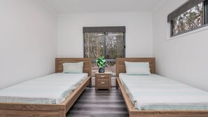 Una camera da letto con due letti in legno, un comodino con cassetti, una pianta in vaso e una finestra vista alberi.