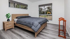 A bedroom with a bed, wooden nightstand, and a window with a view of construction. - Boab Boat n Bush Getaway (Agnes Water)