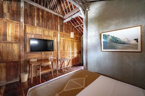 A rustic room with wooden walls, a flat-screen TV, a small table, a chair, and a framed picture on the wall. - Villa Pau Hana (Pecatu)