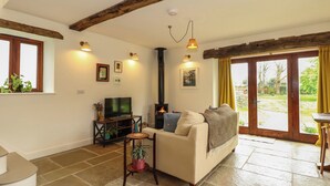 A living room with a sofa, TV, fireplace, and large windows. - The Little Hay Barn (Norwich)