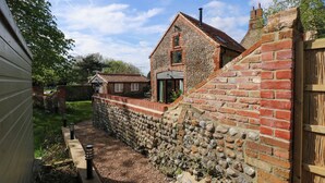 A stone wall with a wooden fence, a brick house with a tiled roof, and a garden area with gravel and plants. - The Little Hay Barn (Norwich)