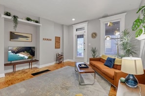Una sala de estar con televisor, sofá, mesa de centro y plantas.