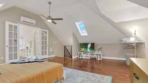A bedroom with a bed, a ceiling fan, a skylight, a TV, and a walk-in closet.