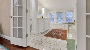 A room with a white door, a window with blinds, a white cabinet, and a patterned rug.