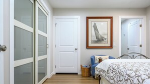A bedroom with a bed, a chair, a wicker basket, and a framed picture on the wall.