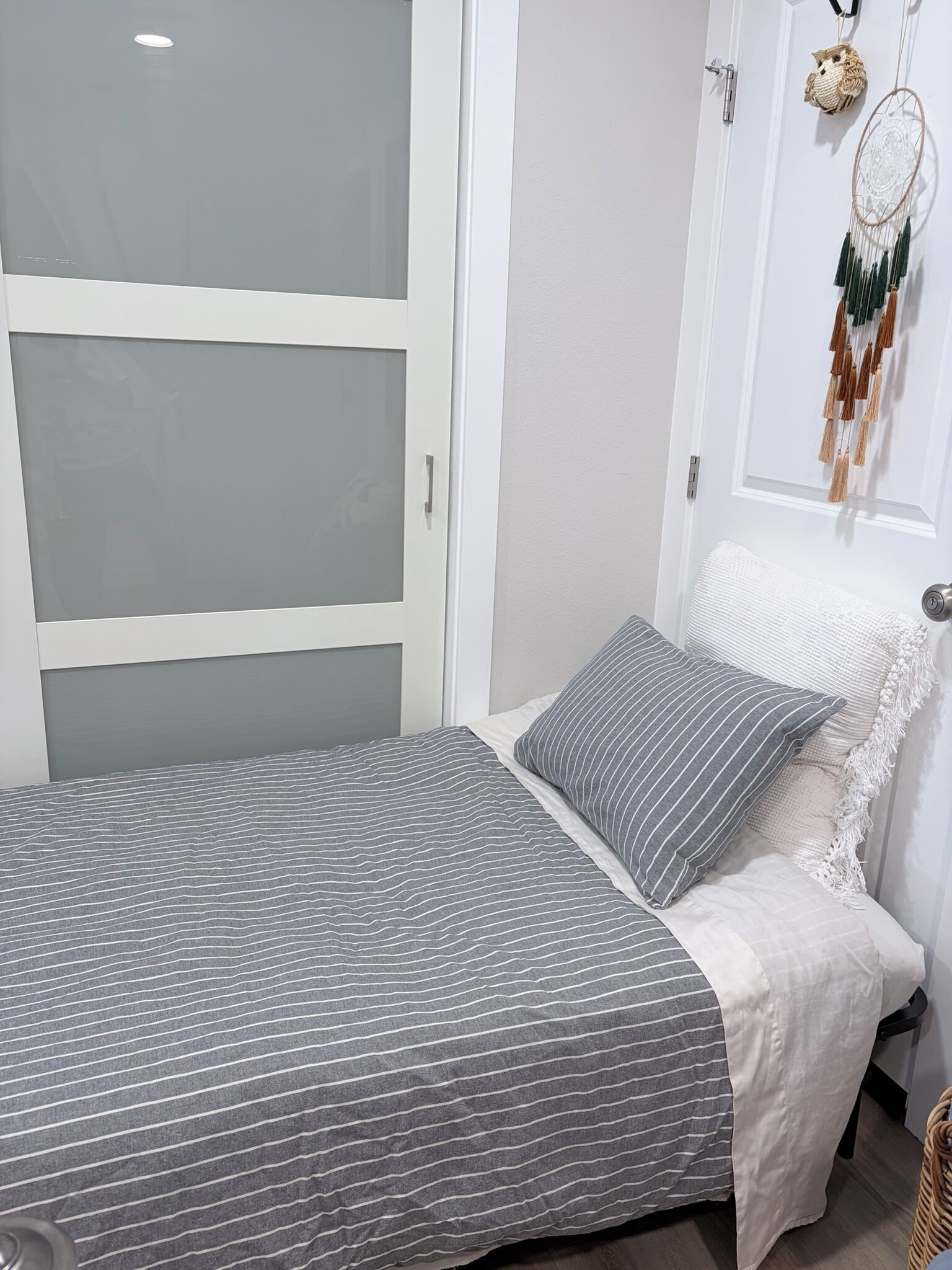 A bedroom with a bed, a wardrobe, and a dreamcatcher on the wall.