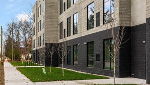Edifici modern d'àmbit elevat, amb façana que combina materials clars i foscos, grans finestres i un jardí ben cuidat amb arbres joves.