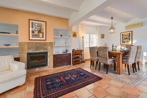 Un salon avec une cheminée, un canapé, une table à manger avec des chaises et un tapis à motifs.