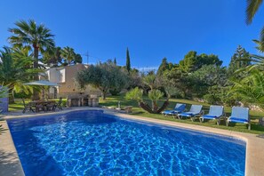 Une piscine à l’eau d’un bleu cristallin, entourée de chaises longues et d’un espace patio aménagé avec une table et des chaises.