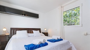 A neatly made bed with white and blue towels, a wooden headboard, and a window with bars. - La Desirada - Javea, Costa Blanca (Javea)