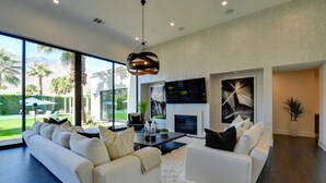 A modern living room with a large sofa set, a fireplace, and a large window overlooking a garden. - Mtn Views + Outdoor Oasis: Palm Springs Home! (Palm Springs)