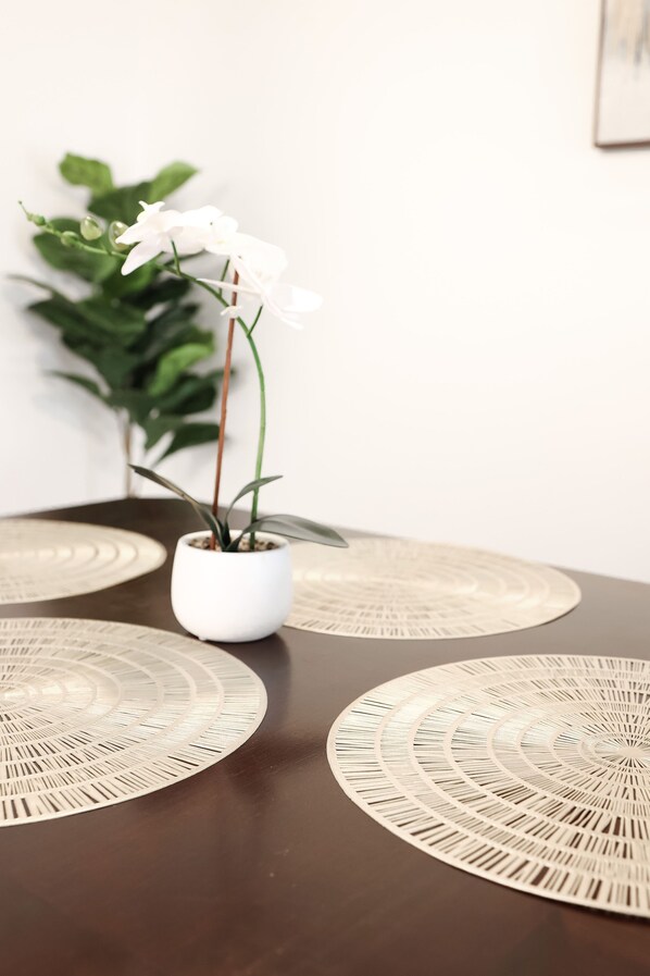 Une table ornée d’une orchidée blanche dans un pot blanc, entourée de sets de table en fibres tressées.
