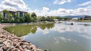 A calm lake with a rocky shoreline, surrounded by buildings and greenery.