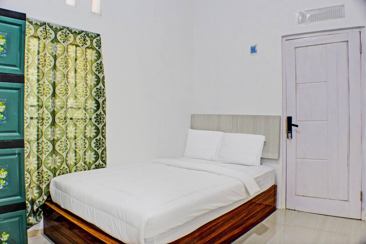 A bedroom with a bed, a wooden headboard, a white door, and a green patterned curtain.