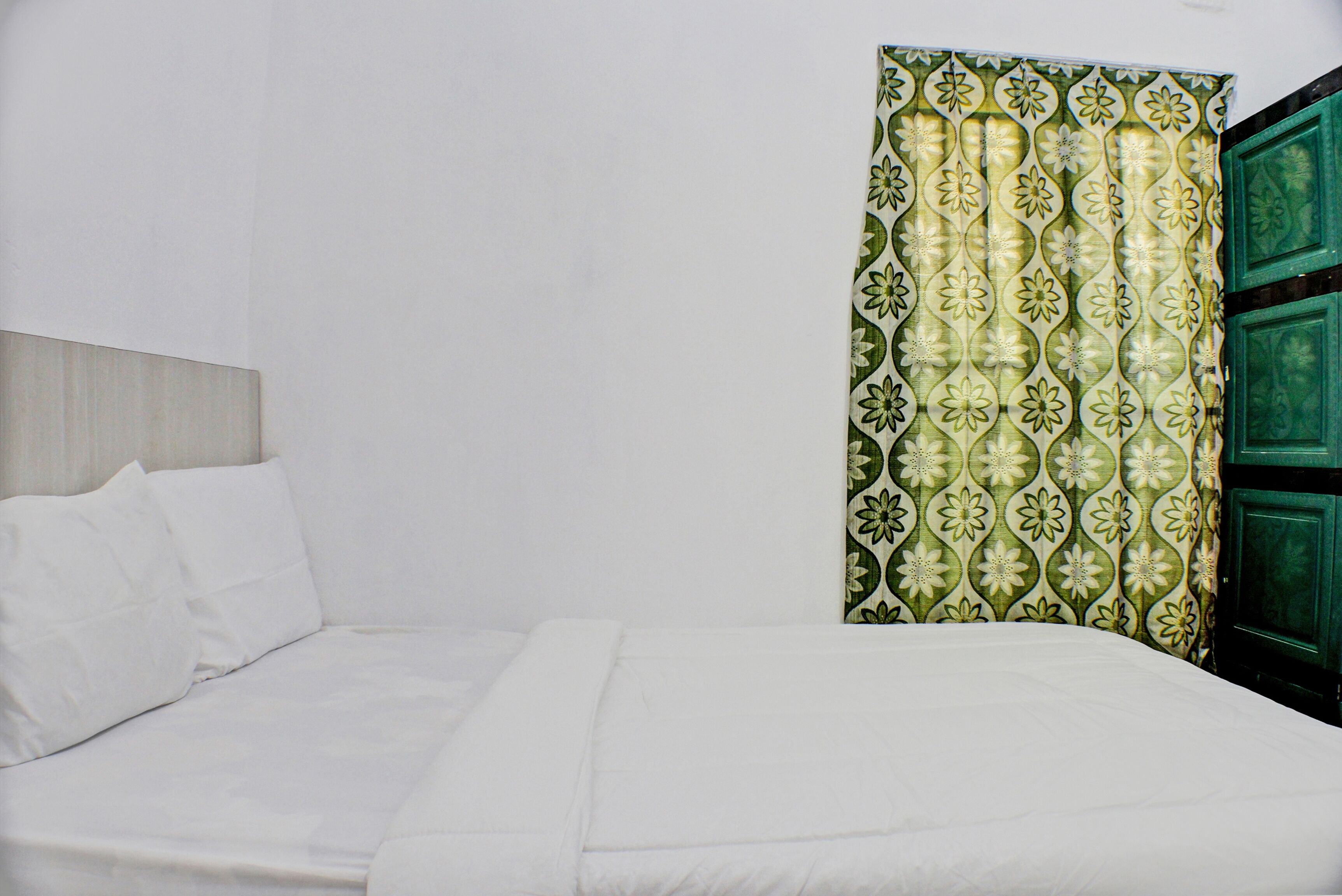 Una cama con ropa de cama blanca, una puerta verde y una pared blanca lisa.