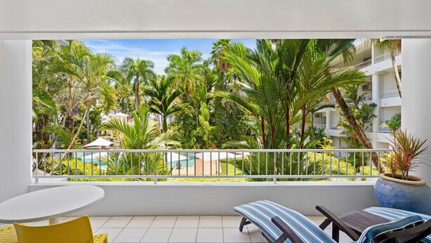 A balcony with a view of a pool surrounded by palm trees and a building with balconies. - Belle Escapes 73 Alamanda Palm Cove (Palm Cove)