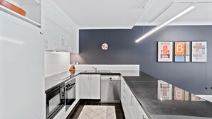 A modern kitchen with white cabinets, a black countertop, and a grey wall with art pieces. - Belle Escapes 73 Alamanda Palm Cove (Palm Cove)