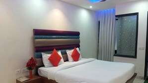 A modern bedroom with a large bed, a headboard with multiple colors, a nightstand, a vase of flowers, and a window with patterned curtains.