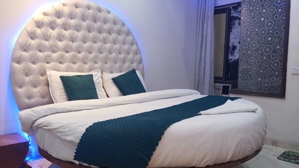 A round bed with a tufted headboard, white bedding, and teal throw pillows.