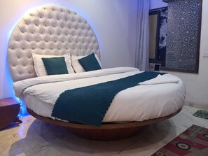 A round bed with a tufted headboard, white bedding, and teal throw pillows. - Hotel Sangam Pacific And Restaurant (Dera Bassi)