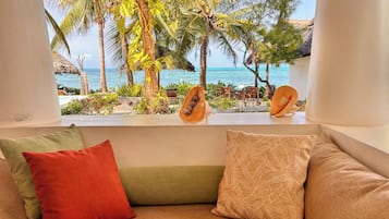 Una habitación con vista a una playa tropical, un alféizar con cocos y una zona de estar con cojines.