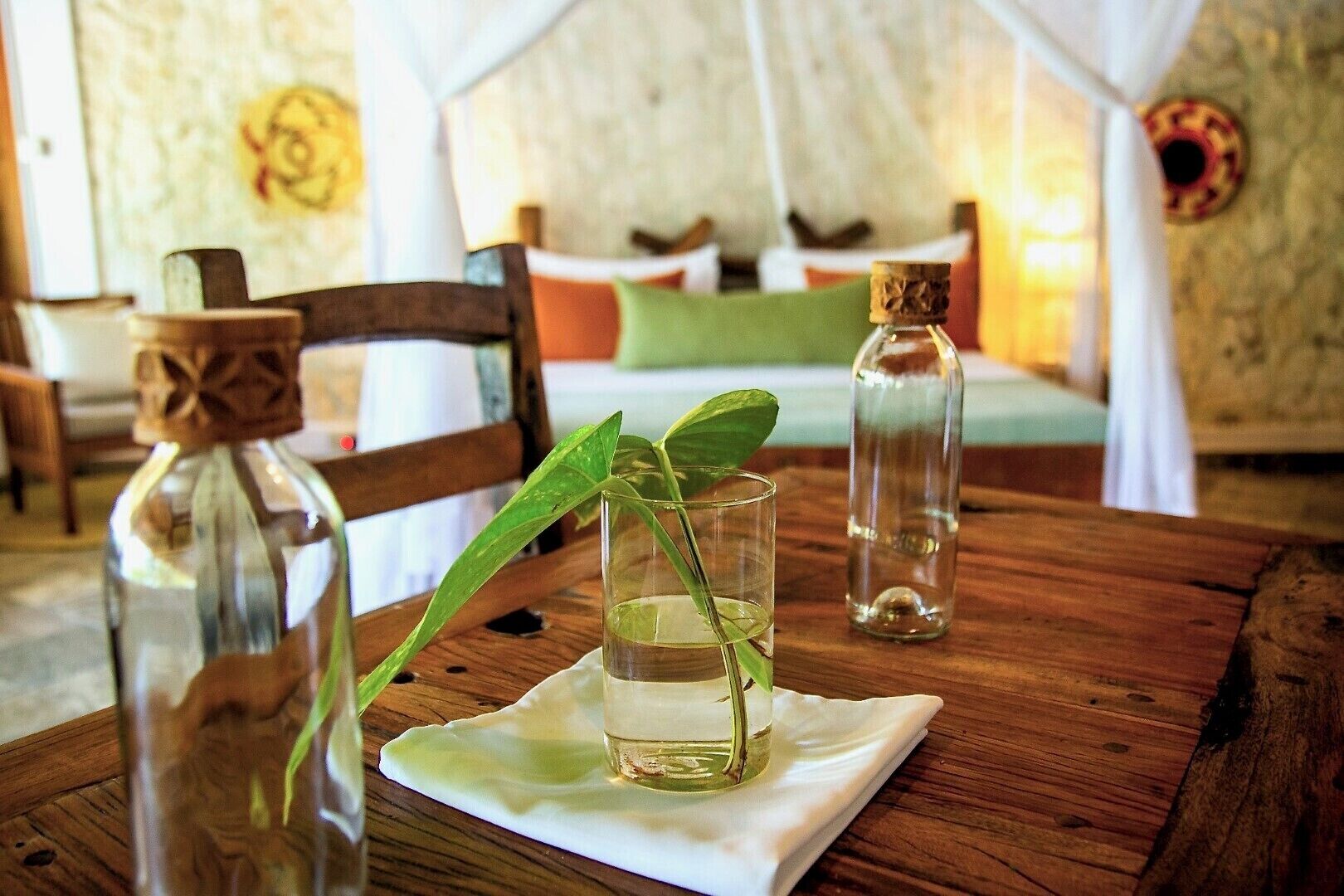 Una mesa de madera con un vaso de agua, una botella y una planta.