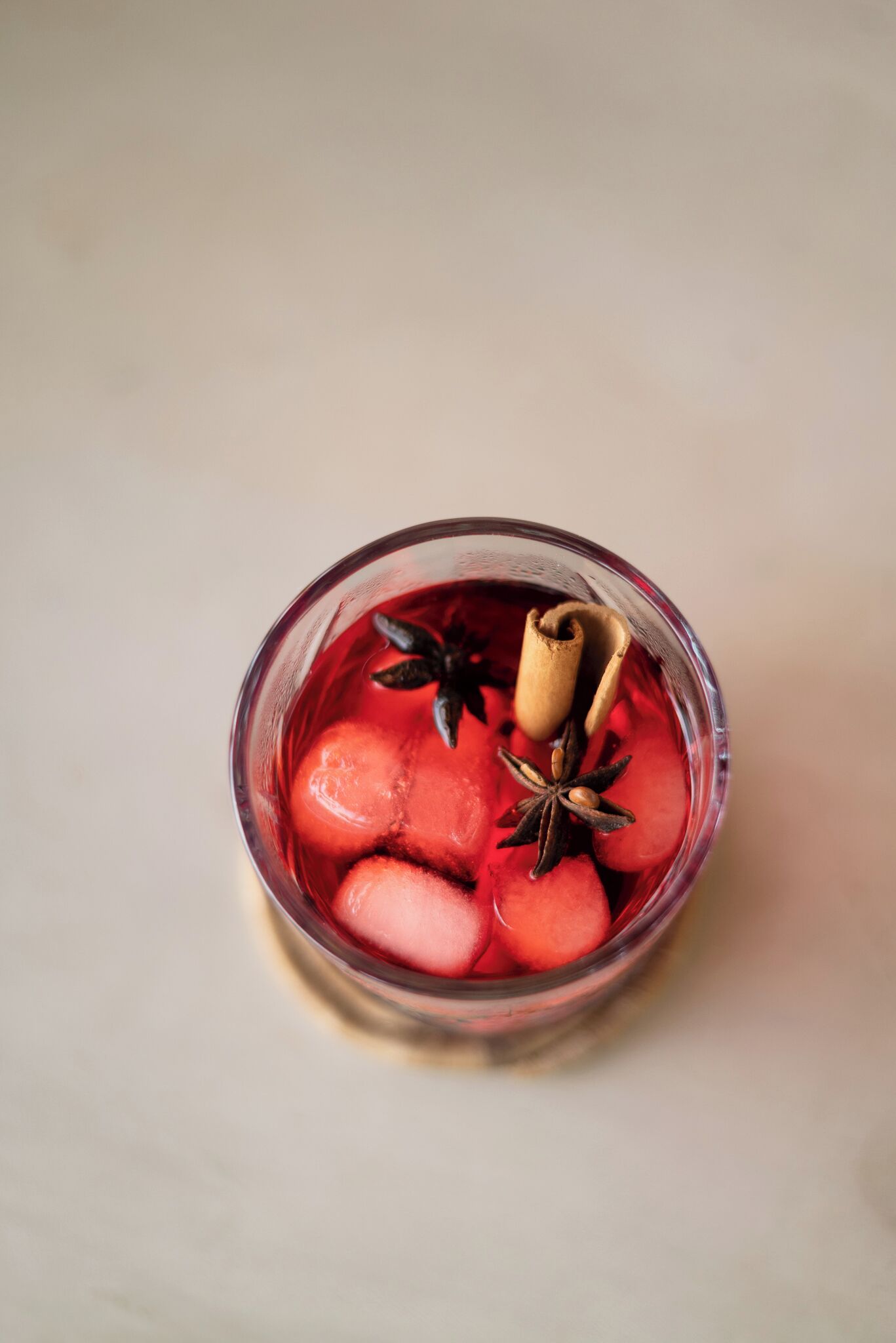 A glass with a red liquid and ice cubes, containing cinnamon sticks and star anise.