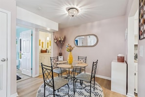 A dining area with a round table, black chairs, a vase with flowers, and a mirror on the wall.