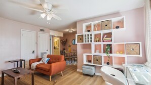 Ein Wohnzimmer mit einer Couch, einem Couchtisch und einem Glastisch. Es gibt eine weiße Regaleinheit mit Dekoration und einen Deckenventilator.