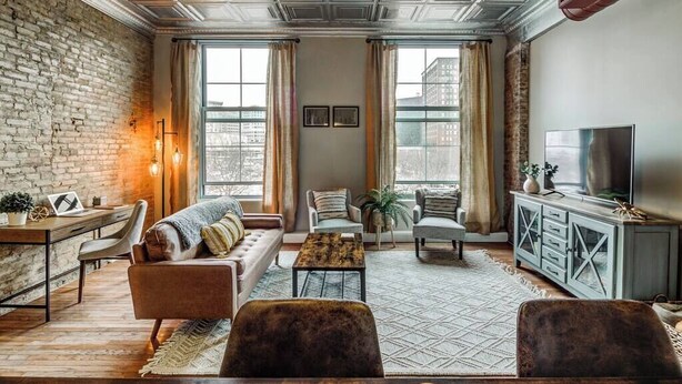A living room with a brick wall, a sofa, a coffee table, a TV, and a cabinet. - Modern Warehouse Loft | Walk to Rock Hall & Stadiums (Cleveland)