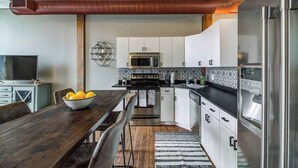A modern kitchen with stainless steel appliances, white cabinets, and a wooden dining table with a bowl of lemons. - Modern Warehouse Loft | Walk to Rock Hall & Stadiums (Cleveland)
