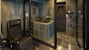 A modern bathroom with a glass-enclosed shower, a black massage chair, and a small vanity with toiletries. - B/C APARTMENT Asakusa Hanazono Dori Hotel with Rental Car and Sauna (Tokyo)