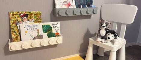 Un espace de jeux pour enfants avec une chaise blanche, une étagère remplie de livres et un jouet coloré.