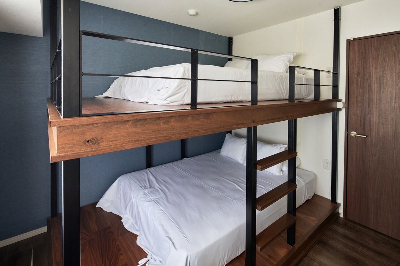 A bunk bed with a wooden frame and white bedding, a door to the right, and a blue wall behind it.