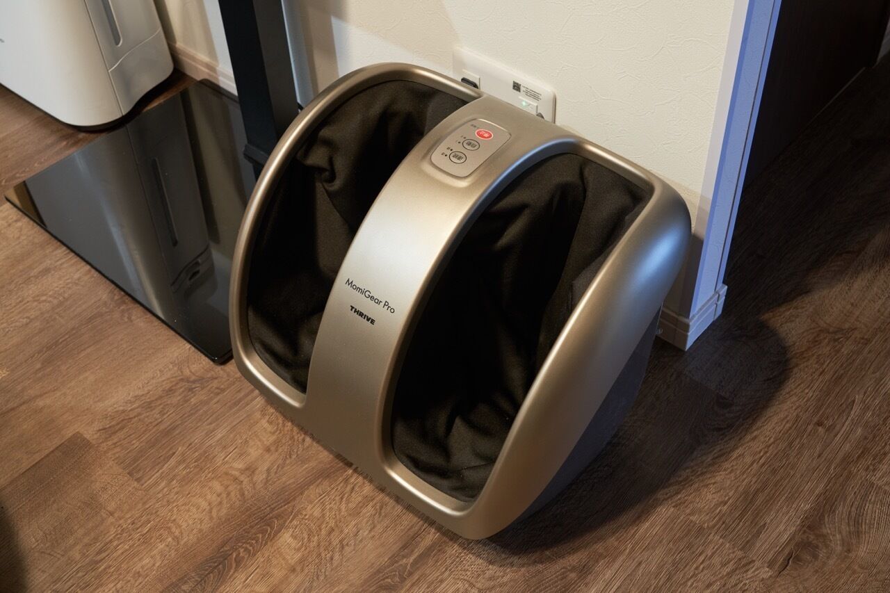 A massage chair labeled 'MomiGear Pro Thrive' in a room with wooden flooring and a white wall.