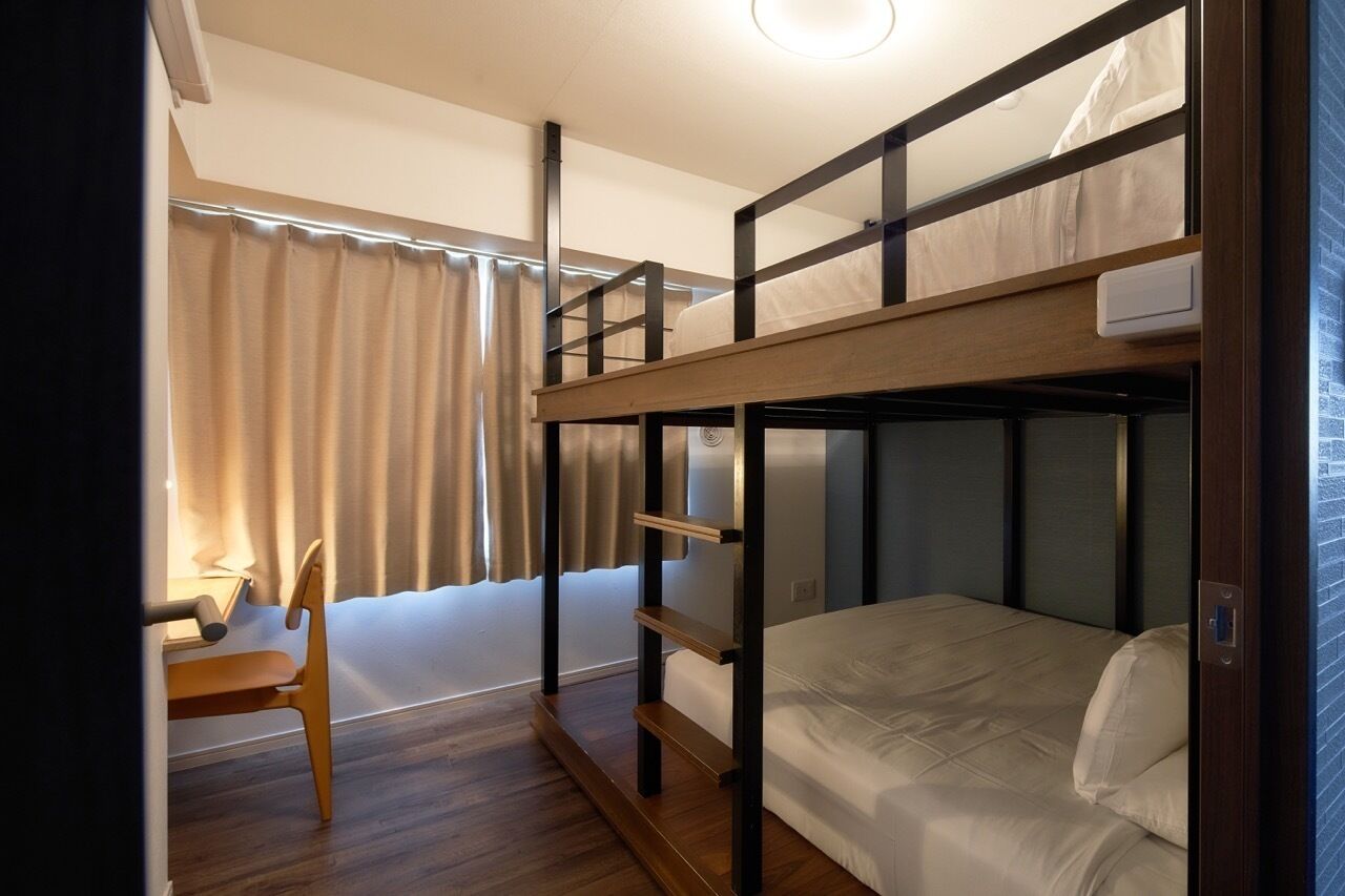A bunk bed room with a desk and chair, a window with curtains, and a wooden floor.
