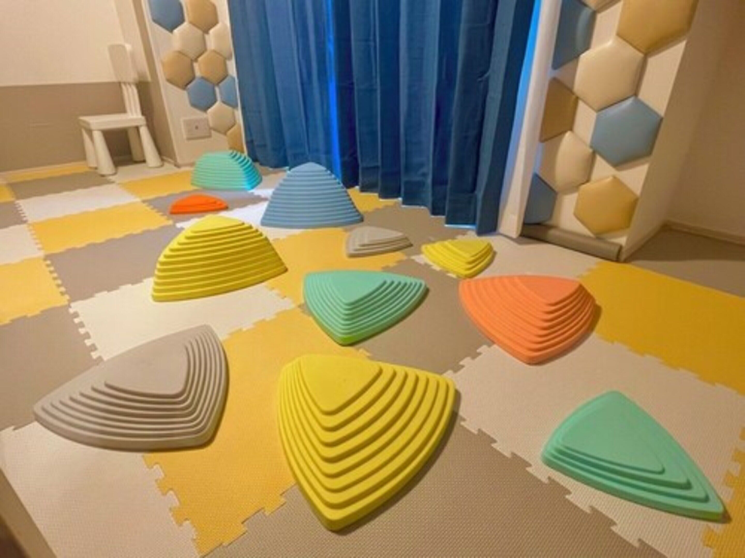 A room with colorful foam mats arranged in a pattern, a chair, and a wall with hexagonal tiles.