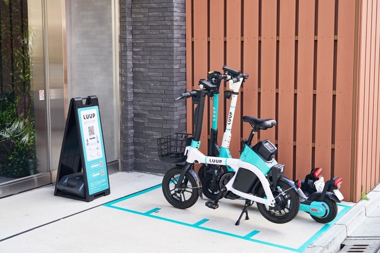 Zwei Elektroroller stehen in einem dafür vorgesehenen Bereich mit einem QR-Code-Schild.