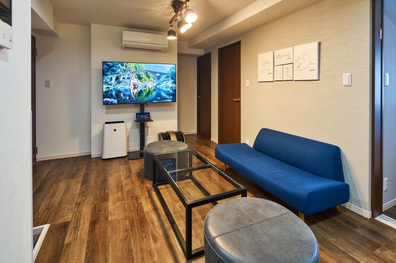 A modern living room with a blue sofa, a glass coffee table, and a flat-screen TV mounted on the wall.