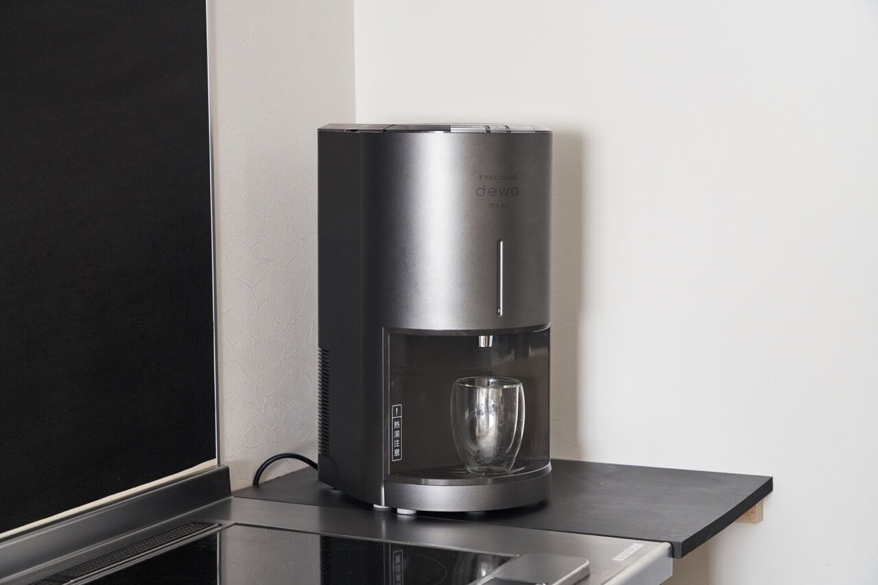 Una elegante cafetera moderna con jarra de vidrio, sobre una encimera negra junto a una pared.