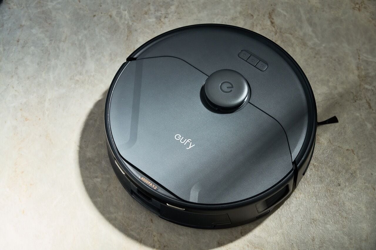 Un aspirateur robot noir, de la marque « Gufy », dont le nom est inscrit sur le couvercle, est posé sur un sol carrelé.