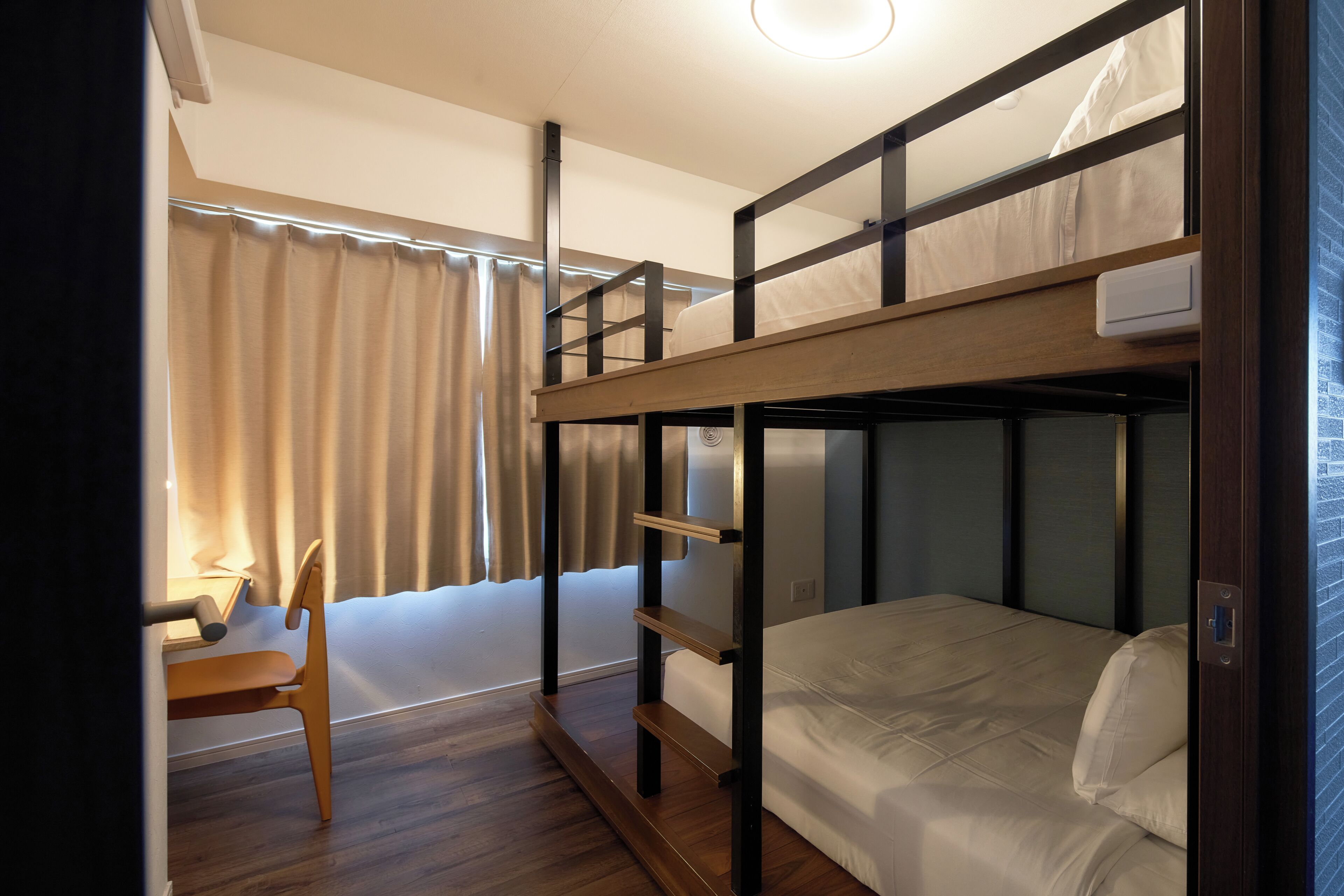 Una camera con un letto a castello, una scrivania e una sedia, una finestra con tende e una luce a soffitto.