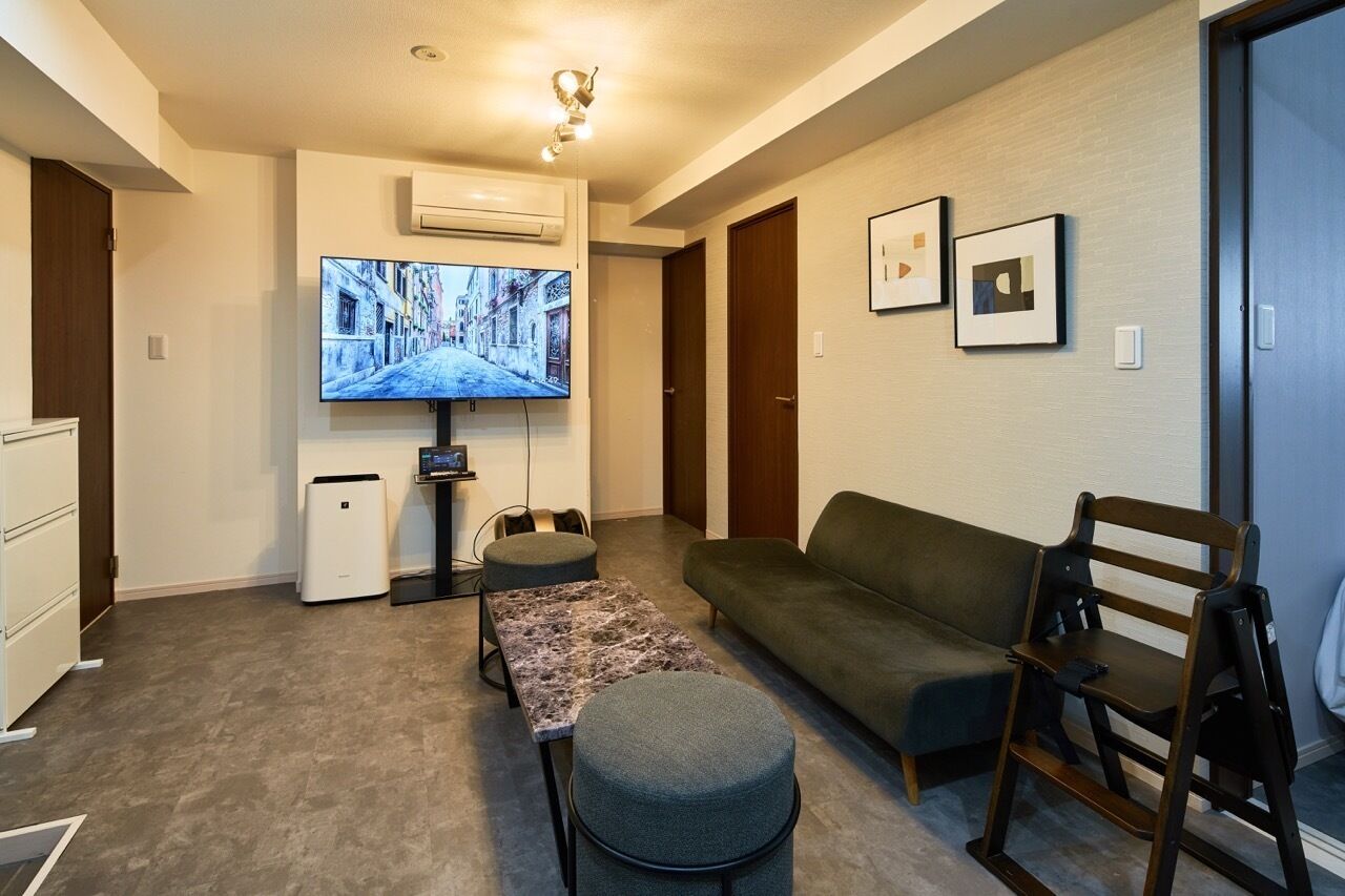 A modern living room with a flat-screen TV, a sofa, a dining table, and a small kitchenette.