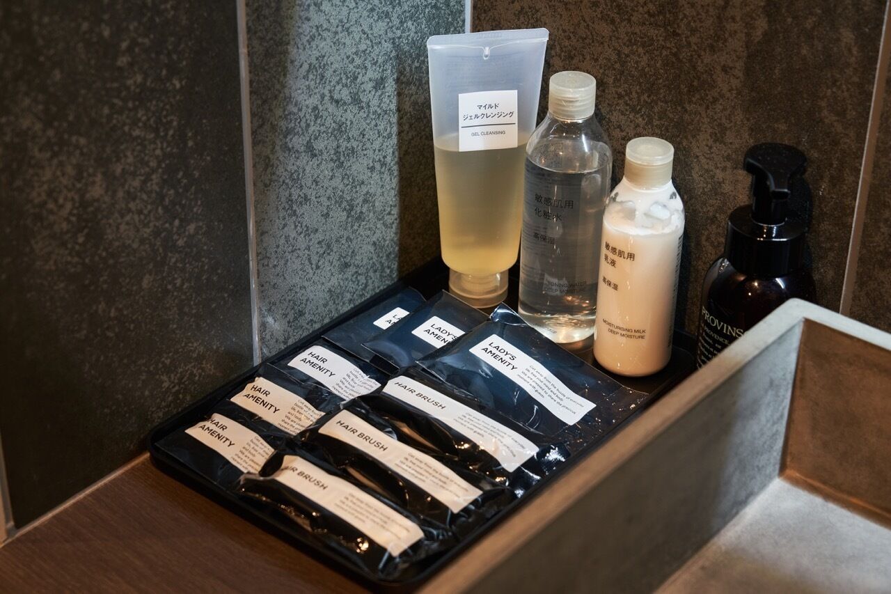 A bathroom counter with various toiletries including a bottle of gel cleansing, a bottle of moisturizing milk, and several hair care products.