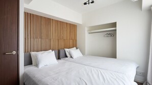 A modern hotel room with two beds, a wooden slat headboard, a coat rack, and a white curtain. - B/C APARTMENT Asakusa Hanazono Dori Hotel with Rental Car and Sauna (Tokyo)