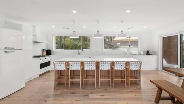 A modern kitchen with white cabinetry, a central island with bar stools, and a wooden bench.